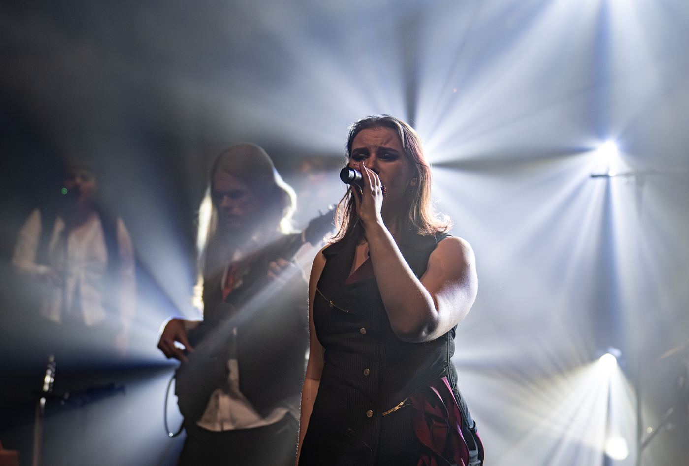 Fifi singing under white stage beams with the band behind her