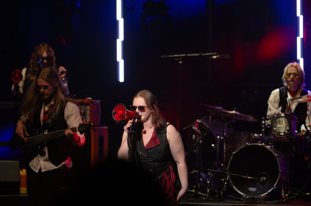 Fifi singing through a red megaphone, with the band around her