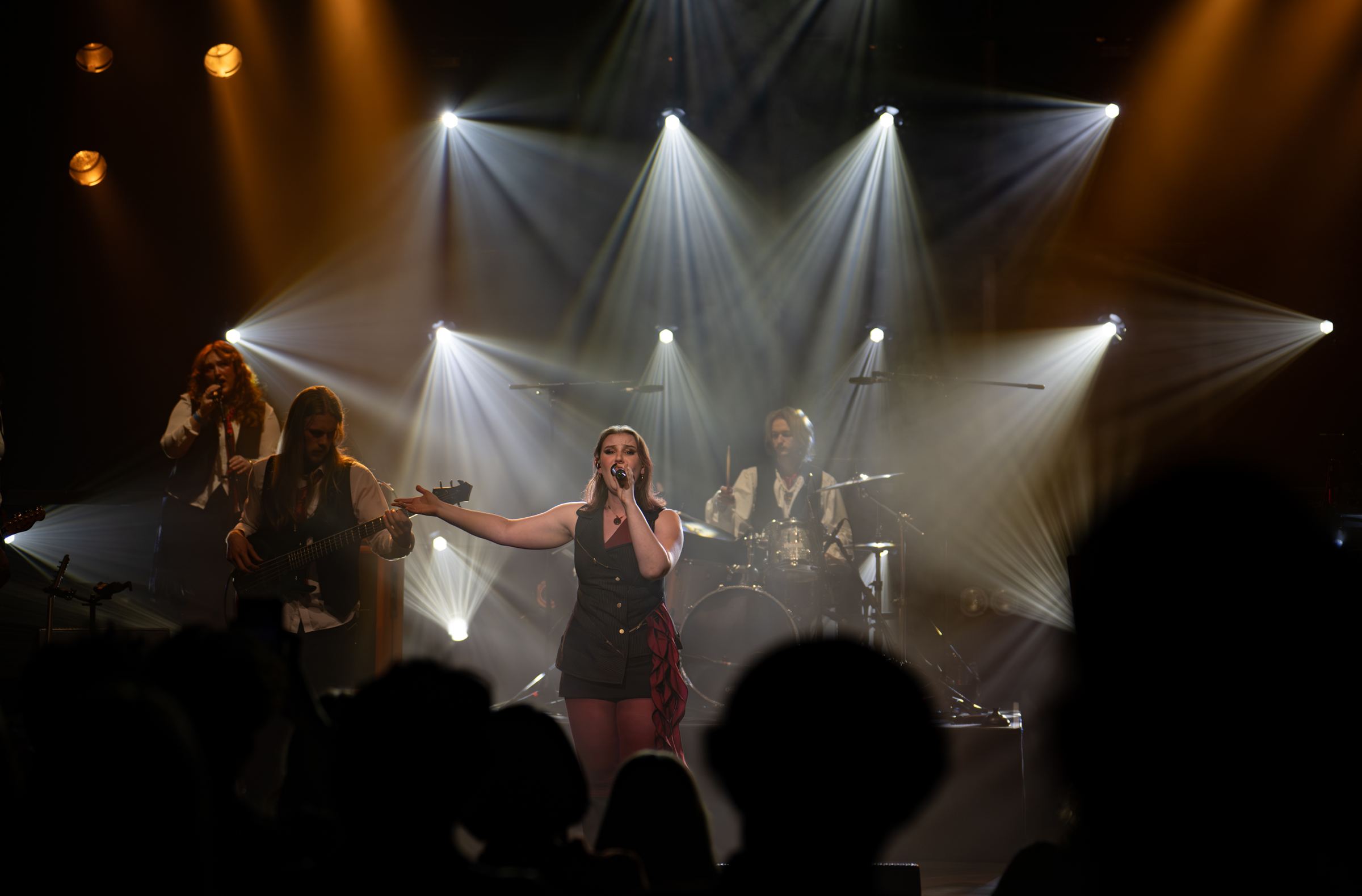 Fifi Tal singing centre stage with her band under white stage lights