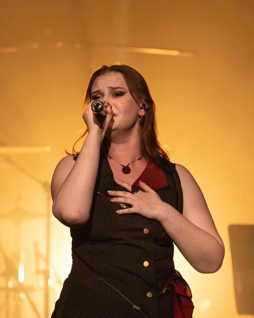 Fifi singing with her hand on her heart in warm amber stage light
